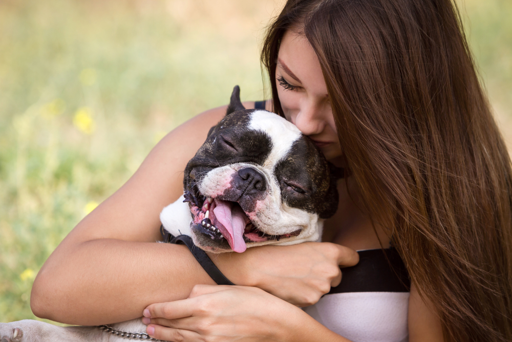 A young woman lovingly embraces a French bulldog with its tongue out and eyes closed, showing the strong bond between pets and their owners – Emergency Vet North Scottsdale